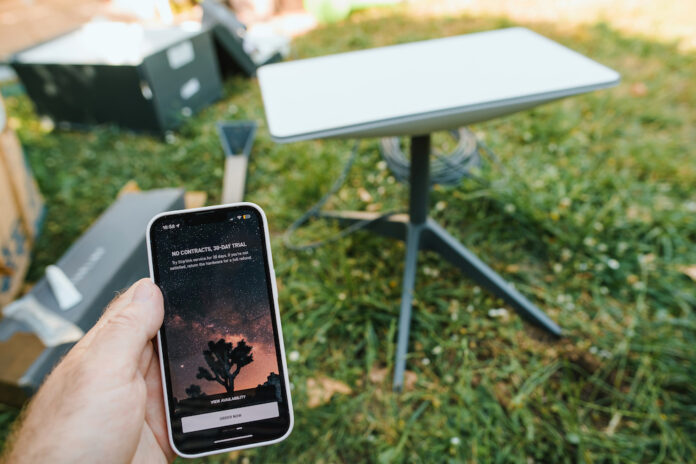 Germany - Jun 16, 2023: Hand holding smartphone with Starlink app setting up dish antenna for reliable satellite transmission. Technology meets nature in front garden.