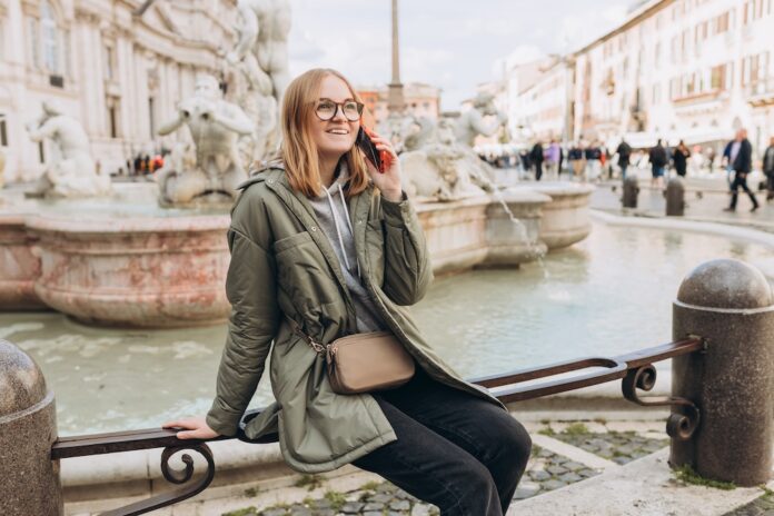 A happy blond woman tourist is standing of the famous Piazza Navona in Rome, Italy. Concept of traveling famous landmarks. Girl with smartphone is walking on a sunny city